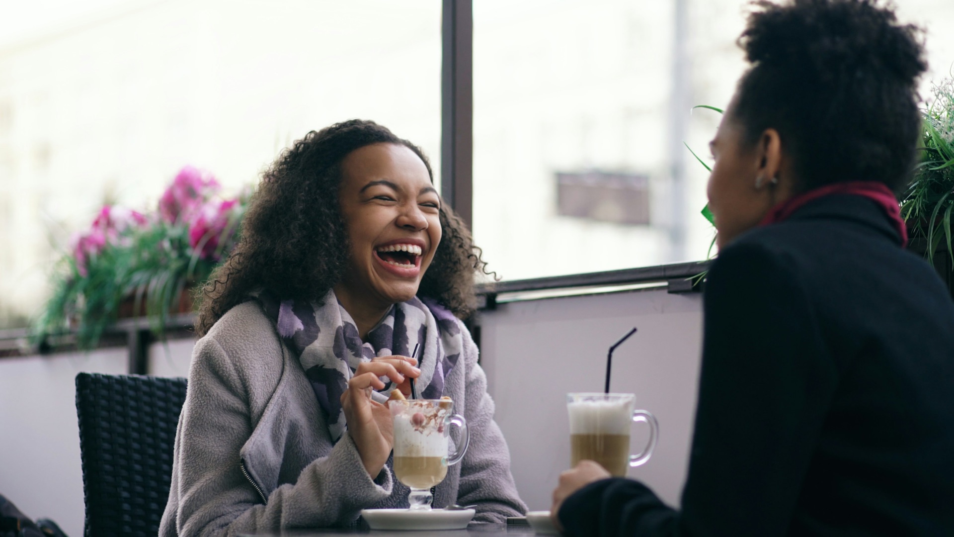 A woman laughing with a friend over coffee